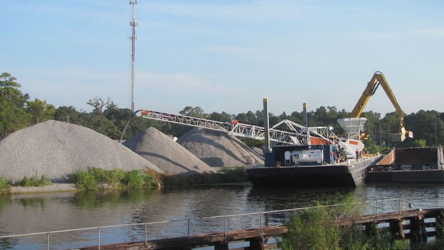 A hopper barge being loaded with aggregate at a riverside dock.