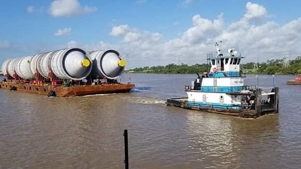 A tug pushing a deck barge loaded with large steel vessels.