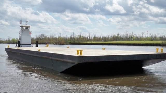 A pushboat moving an empty deck barge along a tree-lined channel.